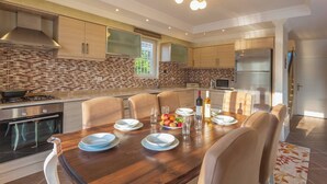 A modern kitchen with a dining area, featuring a wooden table, chairs, and a built-in oven. - Premium 4 Bedroom Villa in Oludeniz (Fethiye)