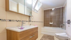 A bathroom with a wooden vanity, a white sink, a mirror, a shower, and a toilet. - Premium 4 Bedroom Villa in Oludeniz (Fethiye)