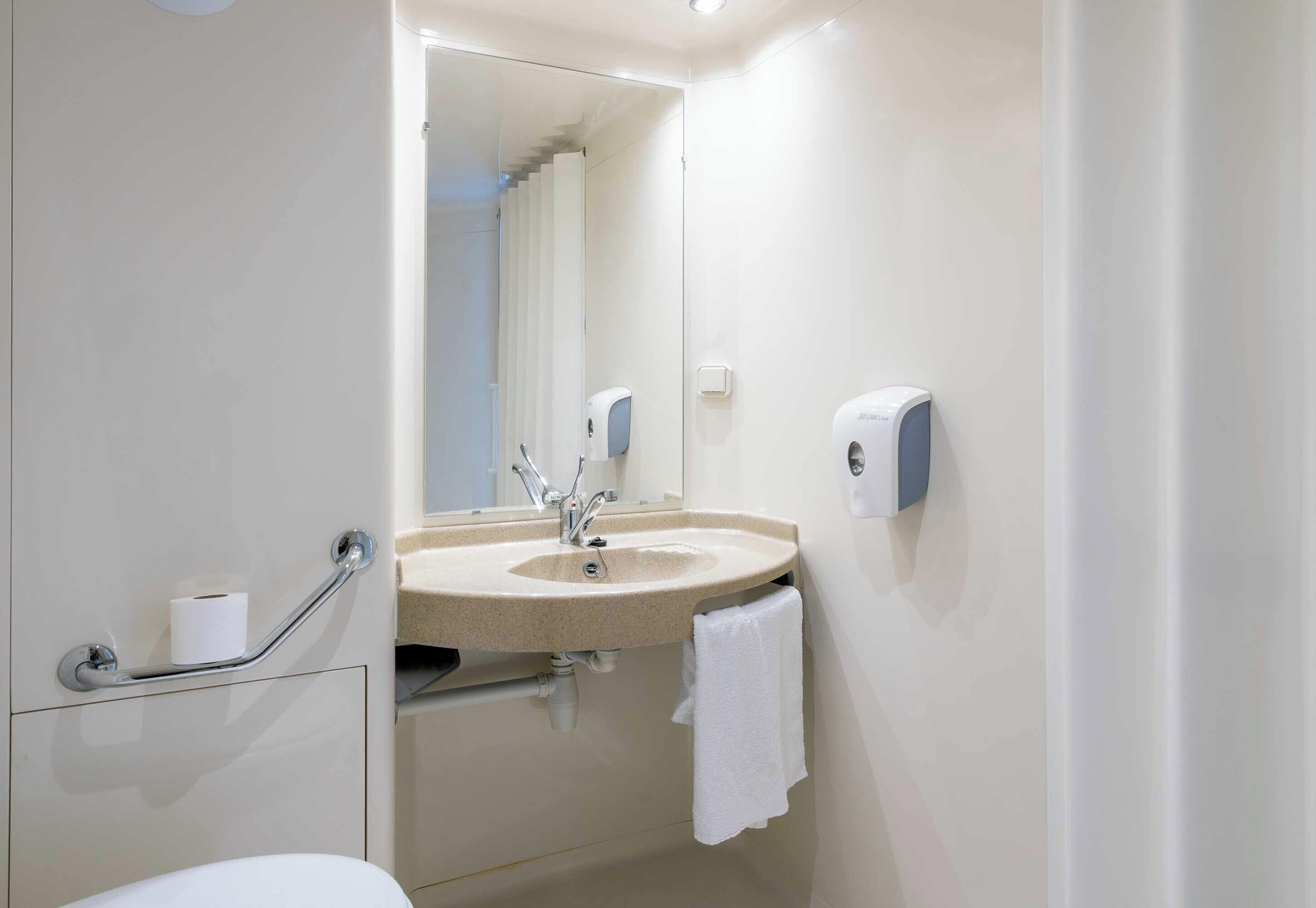 A bathroom with a sink, mirror, towel rack, and hand dryer.