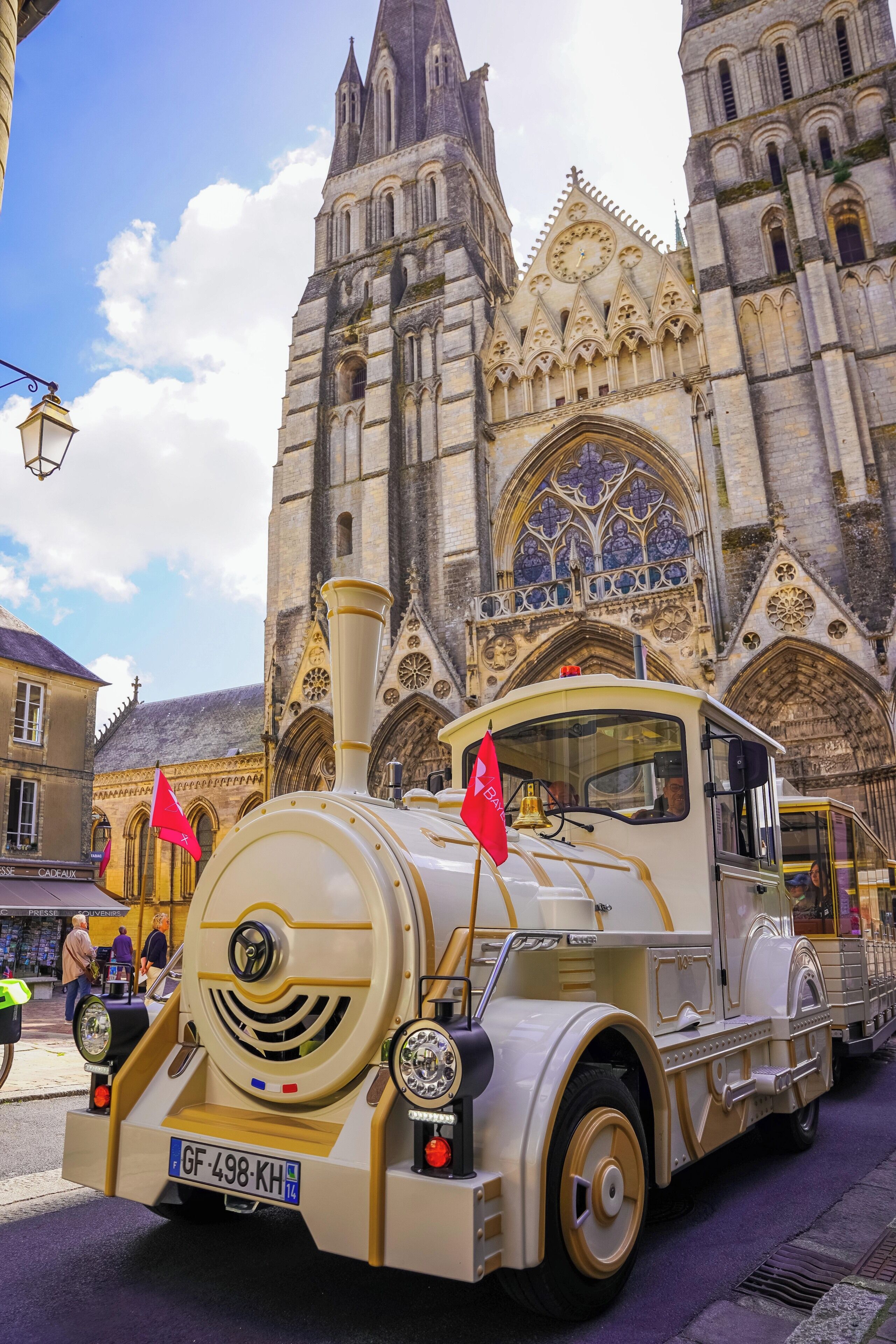 A vintage train with a license plate GF-498-KH parked in front of a Gothic cathedral.