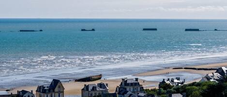 Un pueblo costero con una playa, varios barcos a lo lejos y edificios históricos.