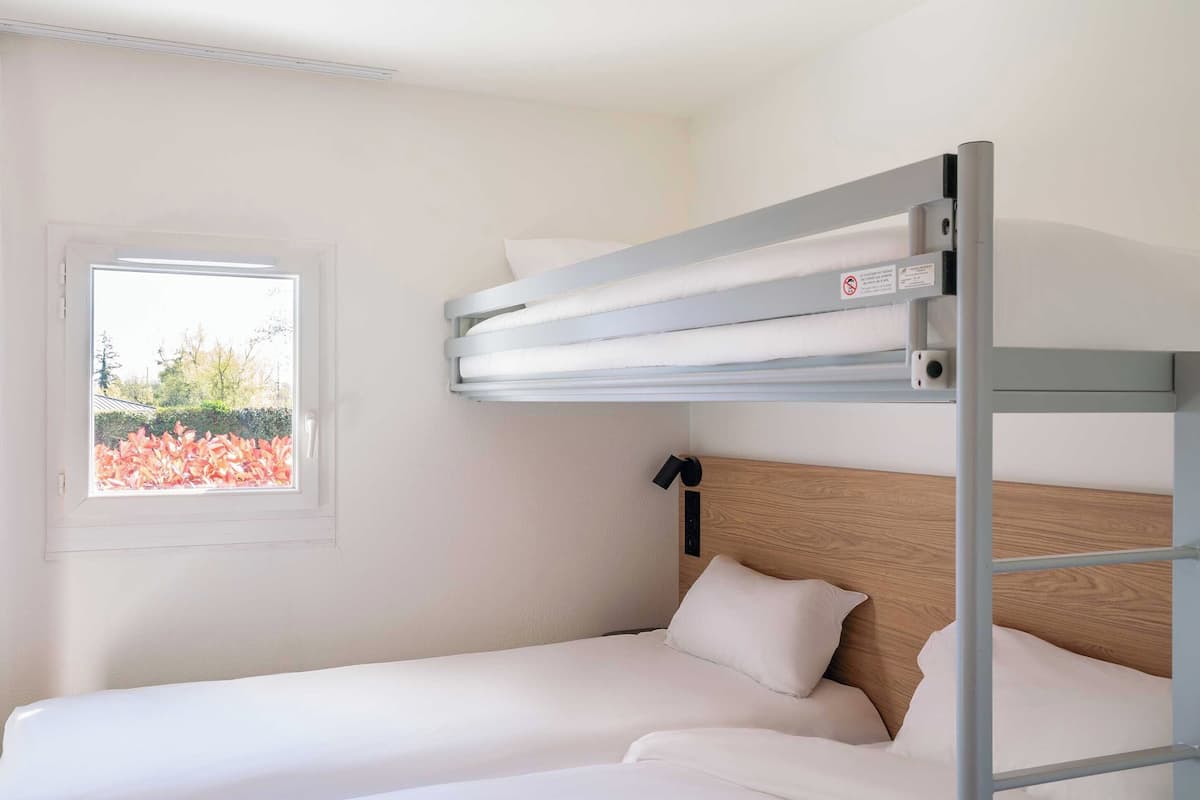Un lit superposé avec une fenêtre, une literie blanche et une tête de lit en bois.