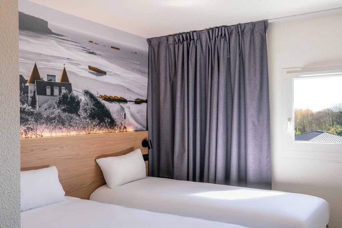 Une chambre d’hôtel avec deux lits, une tête de lit, une grande fenêtre et une fresque murale.