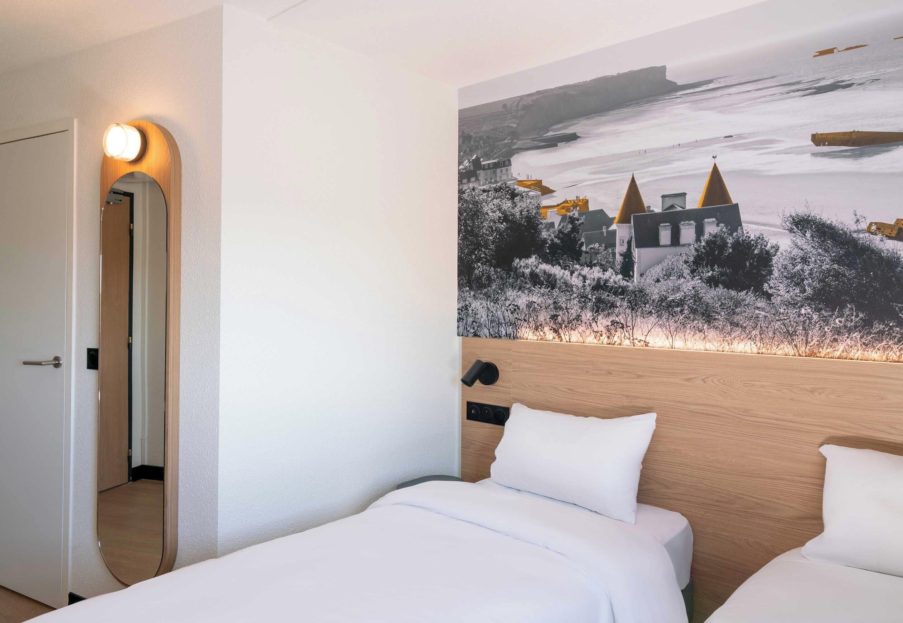 Et hotelværelse med en seng, et træsengegærde, en vægmonteret lampe og et maleri af et slot.