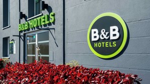 En skylt för ett bed and breakfast-hotell med en symbol för tillgänglighet för rullstolsburna, en grön entré och en röd blomsterrabatt framför.