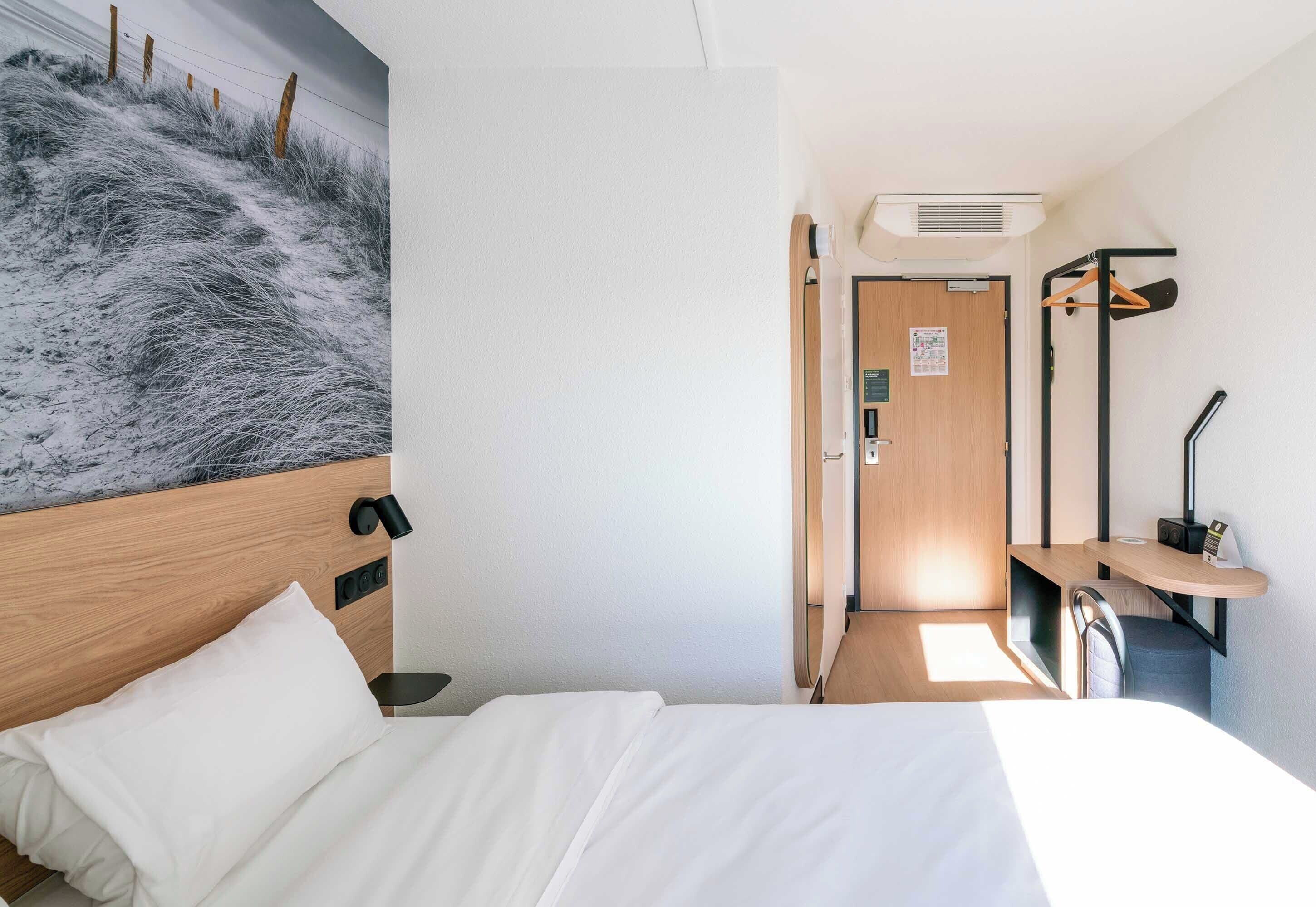 Une chambre d’hôtel comprenant un lit, un bureau, une chaise, un téléviseur fixé au mur et une porte donnant sur une autre pièce.