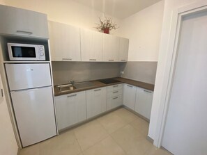 Eine kleine Küche mit Mikrowelle, einem großen Kühlschrank, Spüle und weißen Schränken.