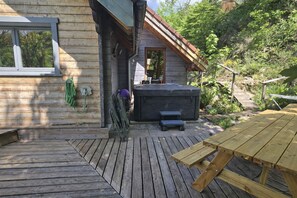 Une terrasse en bois avec un jacuzzi, une table en bois et une fenêtre donnant sur un jardin.
