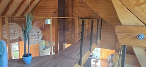 Un intérieur en bois avec un escalier, une plante en pot et une porte vitrée donnant sur l’extérieur.