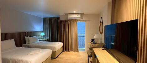 A hotel room with two beds, a desk, a television, and a balcony with curtains.