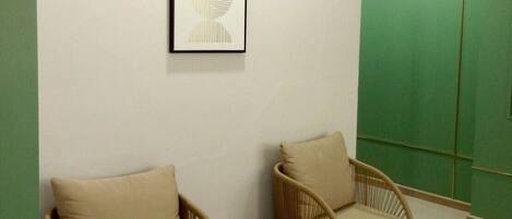 A room with two wicker chairs, a small round table, a framed abstract artwork, and a green partition wall.
