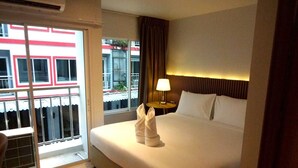 A hotel room with a bed, a nightstand, a lamp, a window with curtains, and a view of buildings outside.