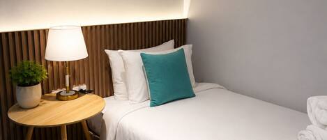 A hotel room with a bed, a bedside table with a lamp, a potted plant, and a chair.