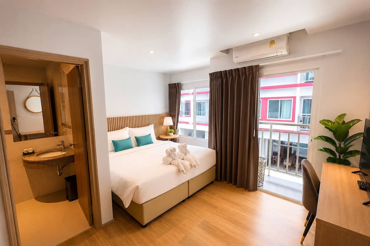 A hotel room with a bed, a desk, a chair, a sink, and a balcony with a view.