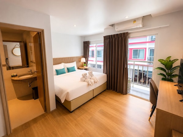 A hotel room with a bed, a desk, a chair, a sink, and a balcony with a view. - Azizi Boutique Hotel (Patong)