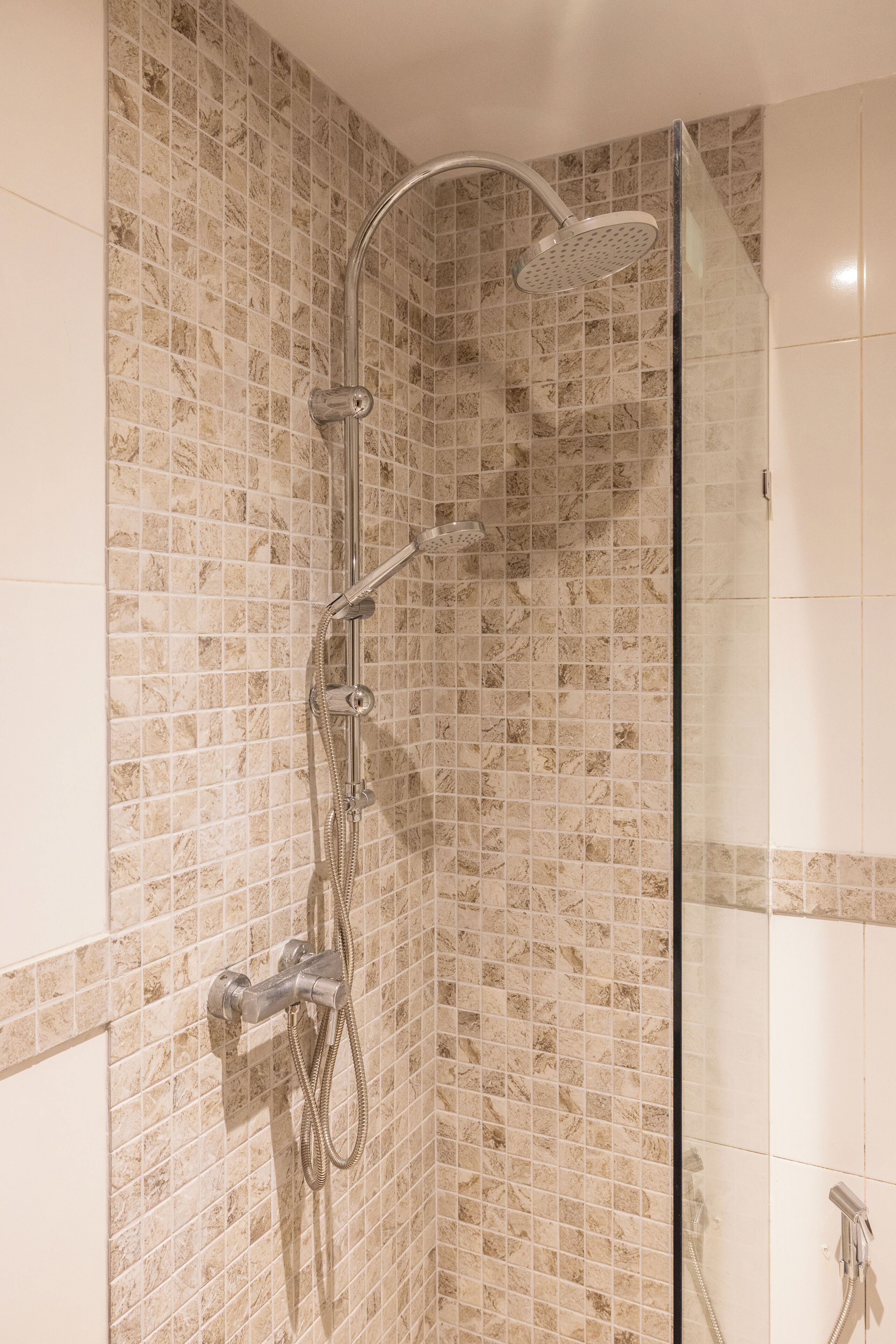 A shower with a handheld showerhead, a wall-mounted faucet, and a glass-enclosed shower area.