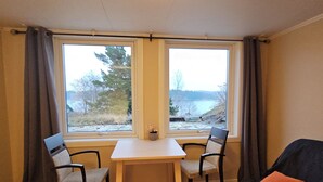A room with a table and two chairs, a couch, and a view of a lake and trees. - Sea Cottages 10 - The First Seaview Apartment (Åkersberga)