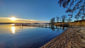 A calm lake with a wooden pier extending into the water, surrounded by trees and a clear sky. - Sea Cottages 10 - The First Seaview Apartment (Åkersberga)