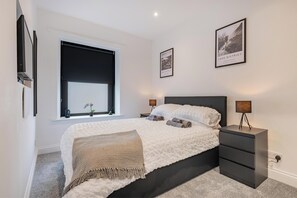 A bedroom with a bed, bedside tables, a window with a blind, and a framed picture on the wall. - Luxury holiday home in Penrith, combining the charm of an old cottage with a sleek, modern interior (Lake District)