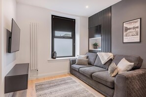 A modern living room with a grey sofa, a patterned rug, a mounted TV, and a framed picture on the wall. - Luxury holiday home in Penrith, combining the charm of an old cottage with a sleek, modern interior (Lake District)