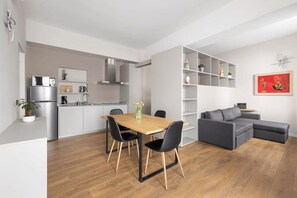 A modern kitchen with a dining area, a grey sofa, and a bookshelf. - 2 min to Lake Maggiore | Modern & Central (Cannobio)
