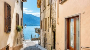 A narrow cobblestone street with buildings on either side, a mountain in the background, and a body of water. - 2 min to Lake Maggiore | Modern & Central (Cannobio)
