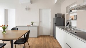 A modern kitchen with a refrigerator, microwave, and sink. There is a dining table with chairs and a vase of flowers. - 2 min to Lake Maggiore | Modern & Central (Cannobio)