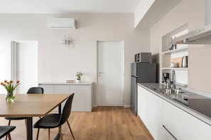 A modern kitchen with a refrigerator, microwave, and sink. There is a dining table with chairs and a vase of flowers. - 2 min to Lake Maggiore | Modern & Central (Cannobio)