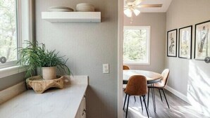 Een moderne keuken met een marmeren aanrecht, een houten plantenstandaard en een eethoek met een tafel en stoelen.