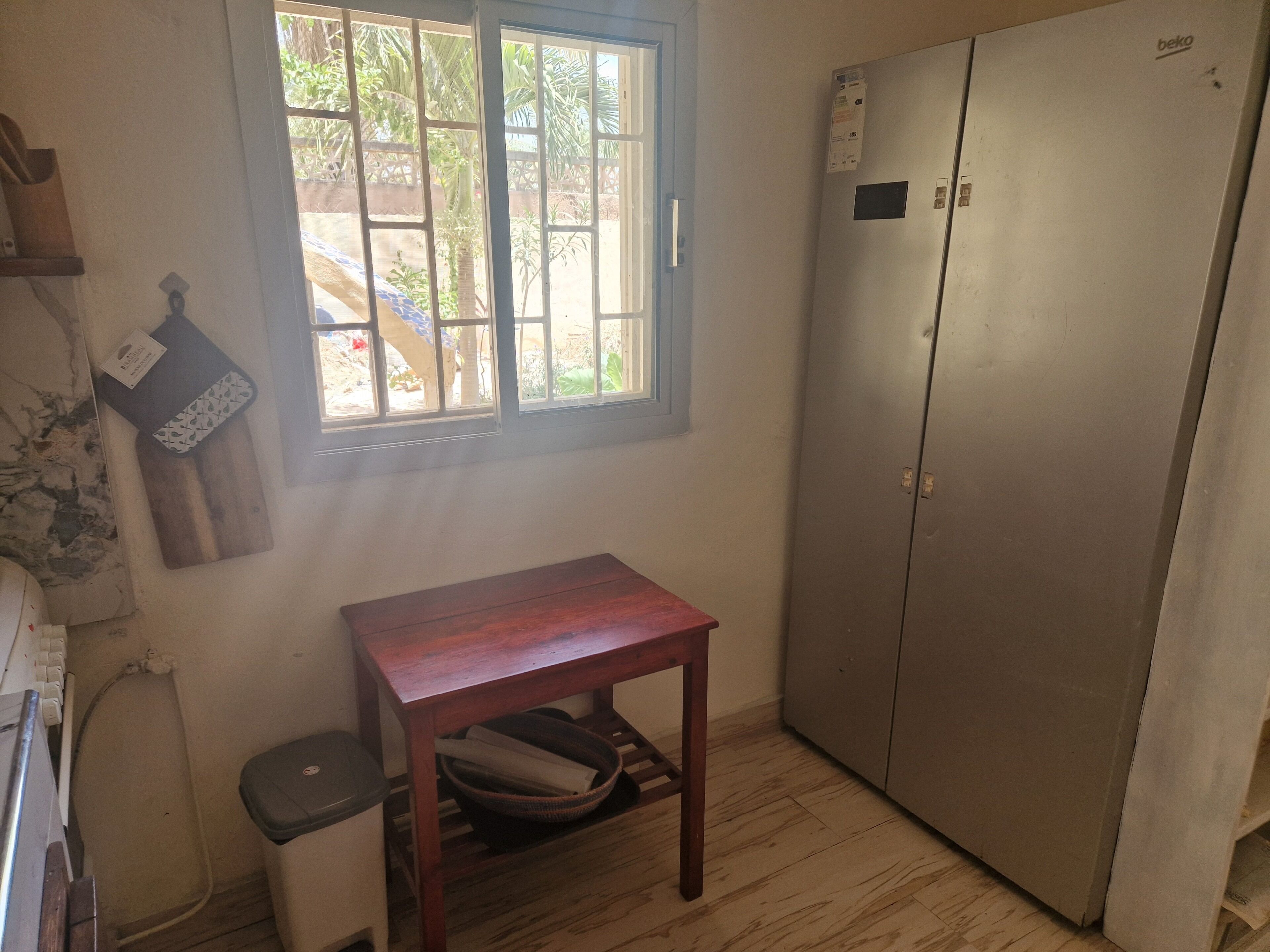 A room with a window, a wooden table, a trash bin, and a large metal cabinet.