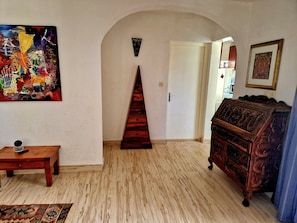 Un couloir avec un escalier en bois, une commode en bois, un tableau accroché au mur et un tapis à motifs.