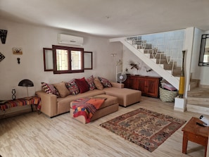 Un salon comprenant un canapé, un tapis à motifs, une table en bois, un escalier et un climatiseur fixé au mur.
