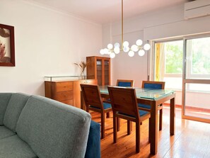 Ein Essbereich mit einem Glastisch, Holzstühlen, einem Schrank und einer Pendelleuchte.