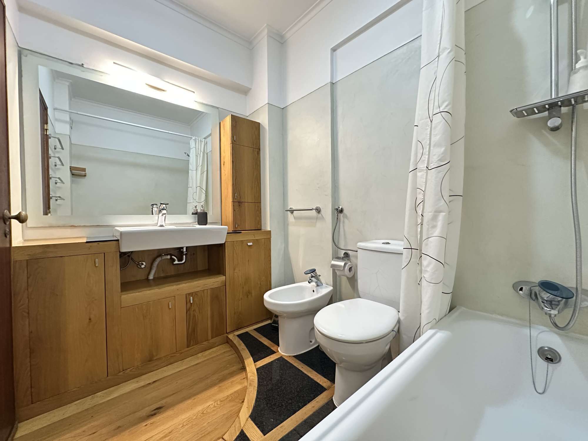 Ein modernes Badezimmer mit einem Holzboden, einem Waschbecken, einer Toilette und einer Duschkabine.