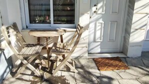 Une terrasse avec une table et des chaises en bois, une porte-fenêtre coulissante et une porte blanche avec une boîte aux lettres.