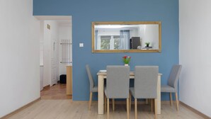 A dining area with a table and four chairs, a mirror on the wall, and a door leading to another room. - Cozy Apartment for Friends | Great Location Close to the Metro (Warszawa)