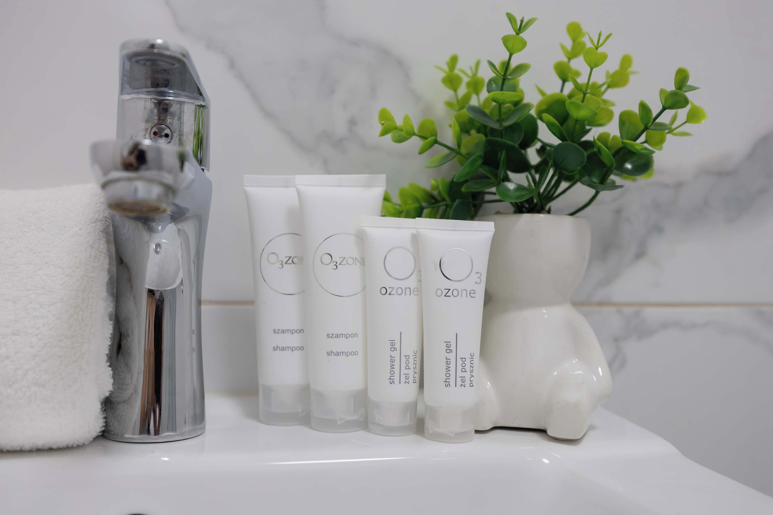 A bathroom with a white towel, a showerhead, and four Ozone brand shower gel tubes.