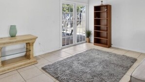 Ein Zimmer mit Holzbalkendecke, einer Glastür, die nach draußen führt, einem Holzregal und einem grauen Teppich.