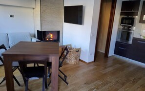 A modern living room with a wooden table, a sofa, a fireplace, a TV, and a kitchen area with an oven and microwave. - Relax Pescasseroli For Ever (Abruzzo)