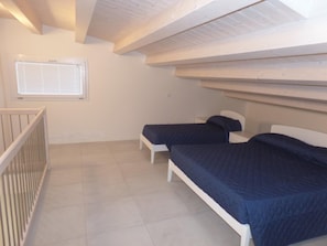 Ein Zimmer mit zwei Betten, einem Fenster mit Jalousien, einem weißen Geländer und einer geneigten Decke.