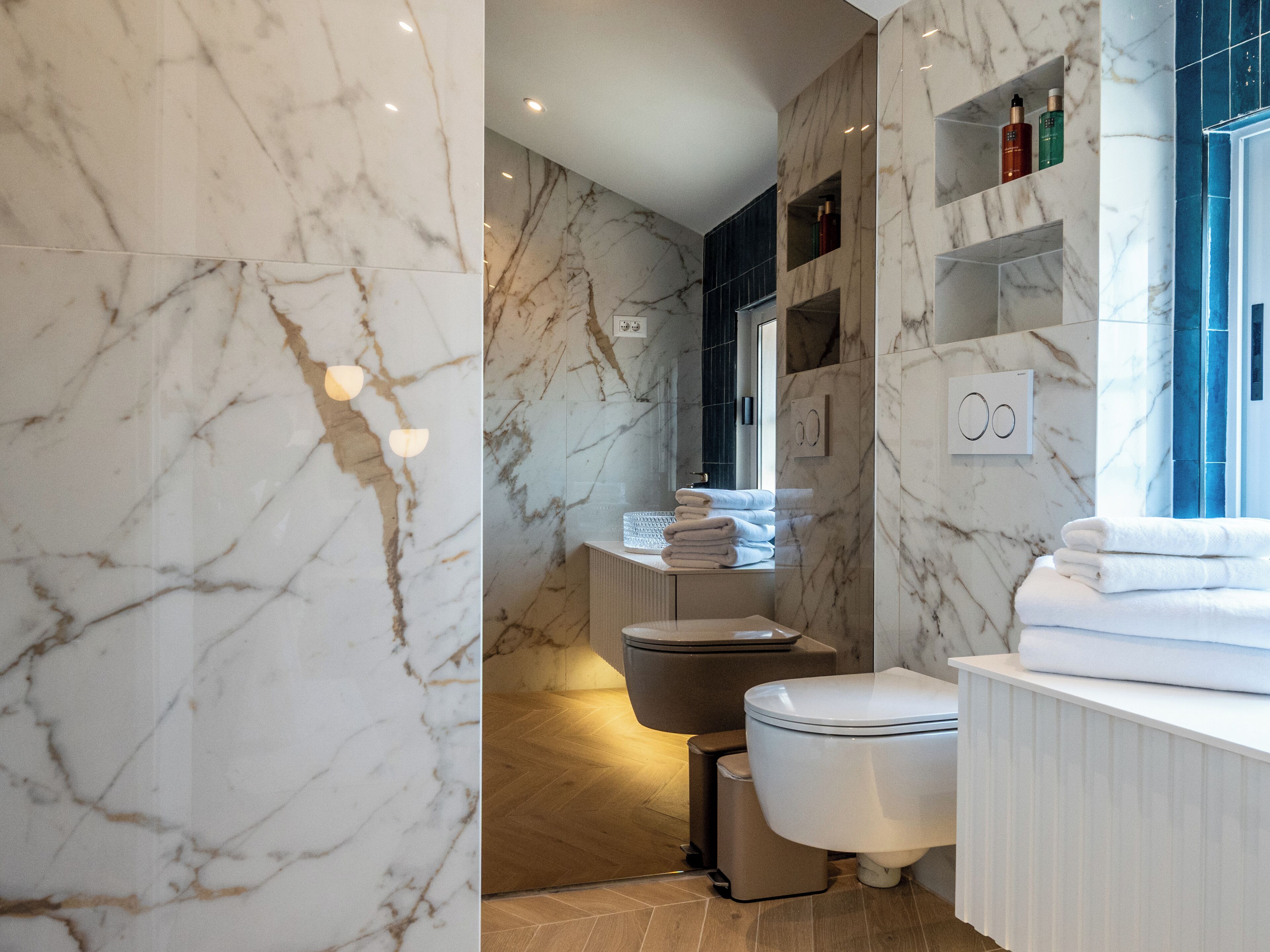 Et badeværelse med marmorvægge, en hvid vask, et toilet og et bruseområde.