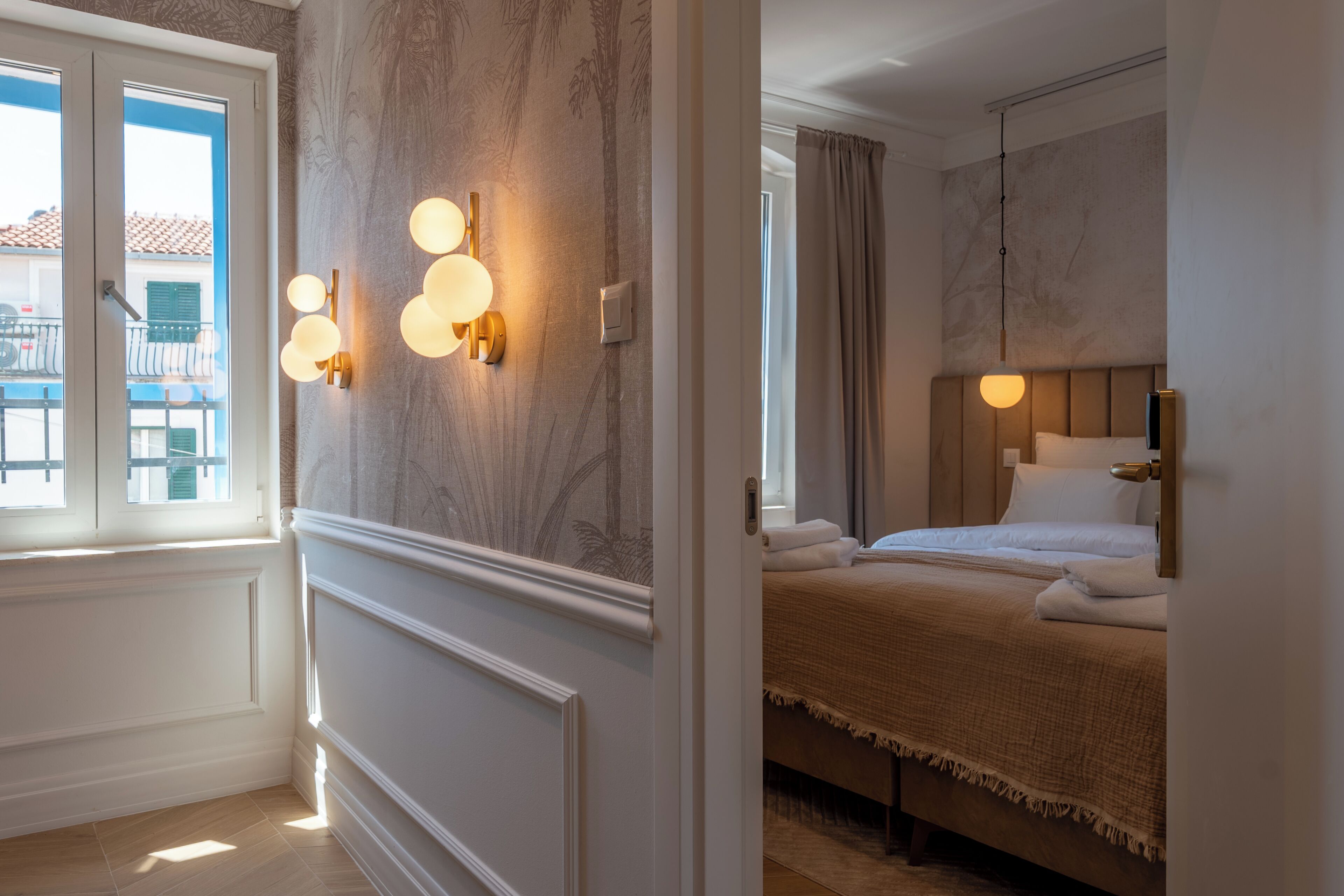 A hotel room with a bed, wall sconces, a window, and a view of the outside.