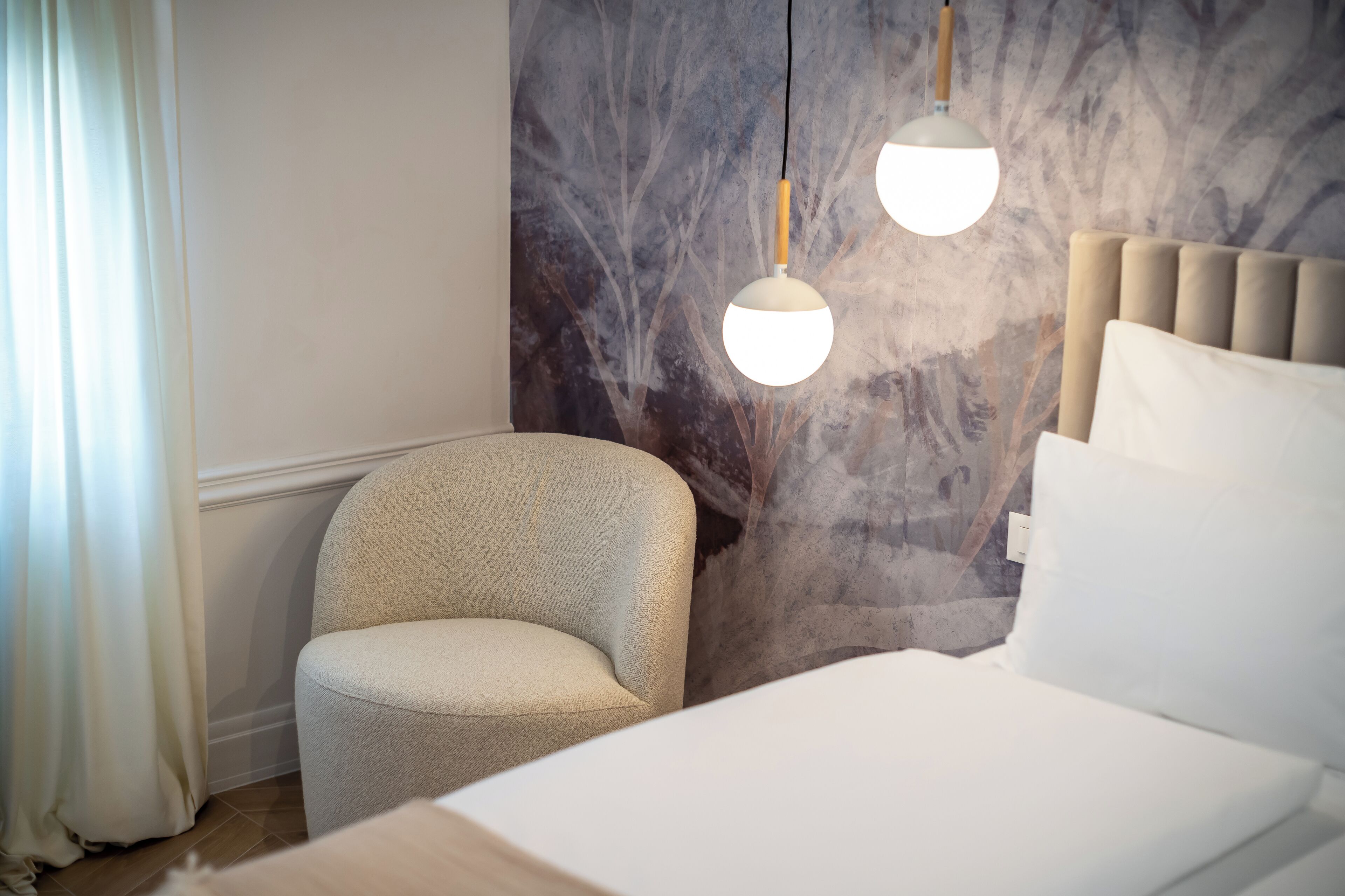 A bedroom with a bed, a chair, and a wall with a tree mural.