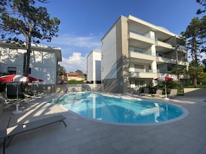 Ein modernes Gebäude mit Schwimmbad, Liegestühlen und Sonnenschirmen.