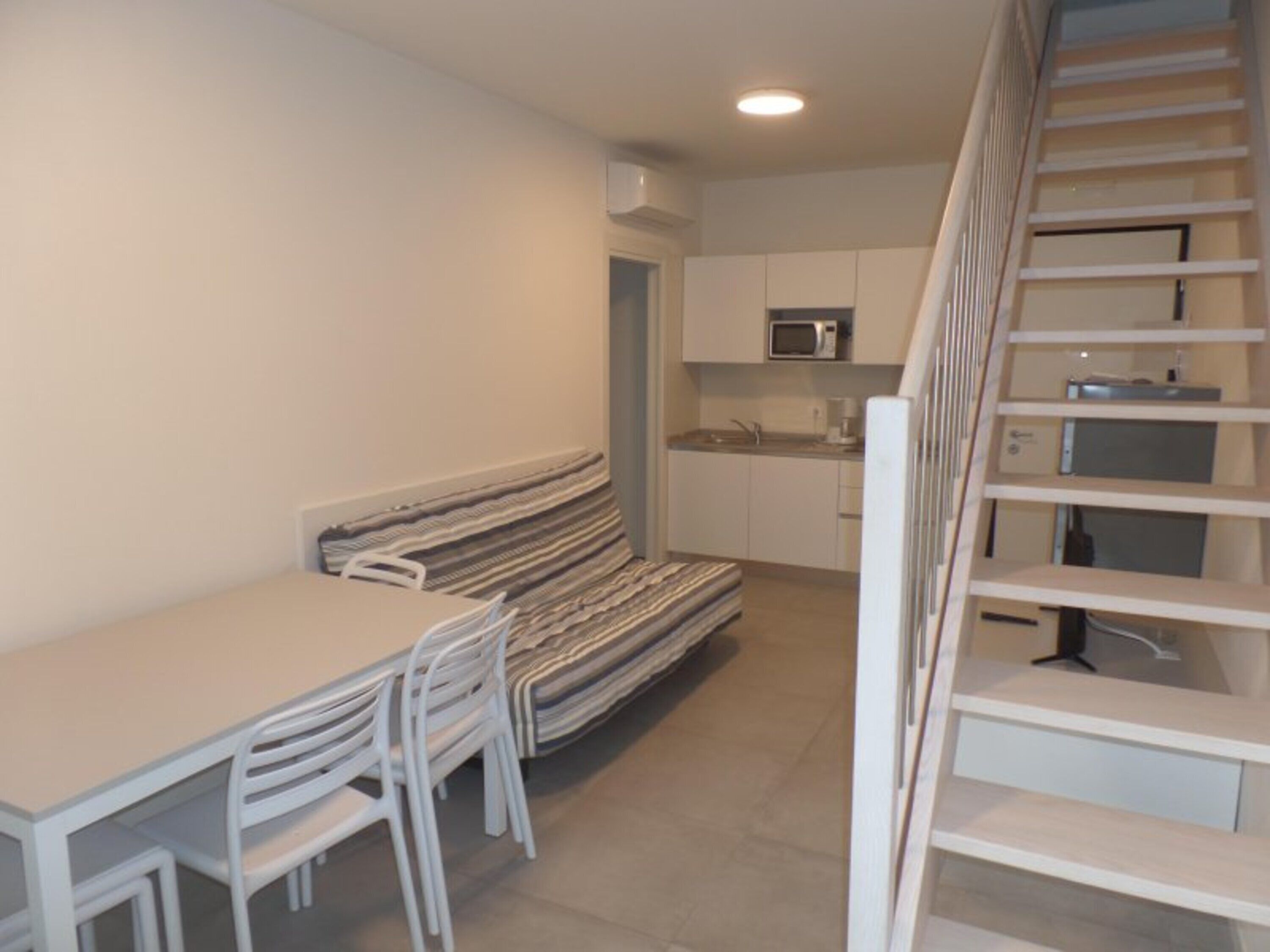 A compact kitchen with a microwave, a small sink, and a staircase leading to a loft area.