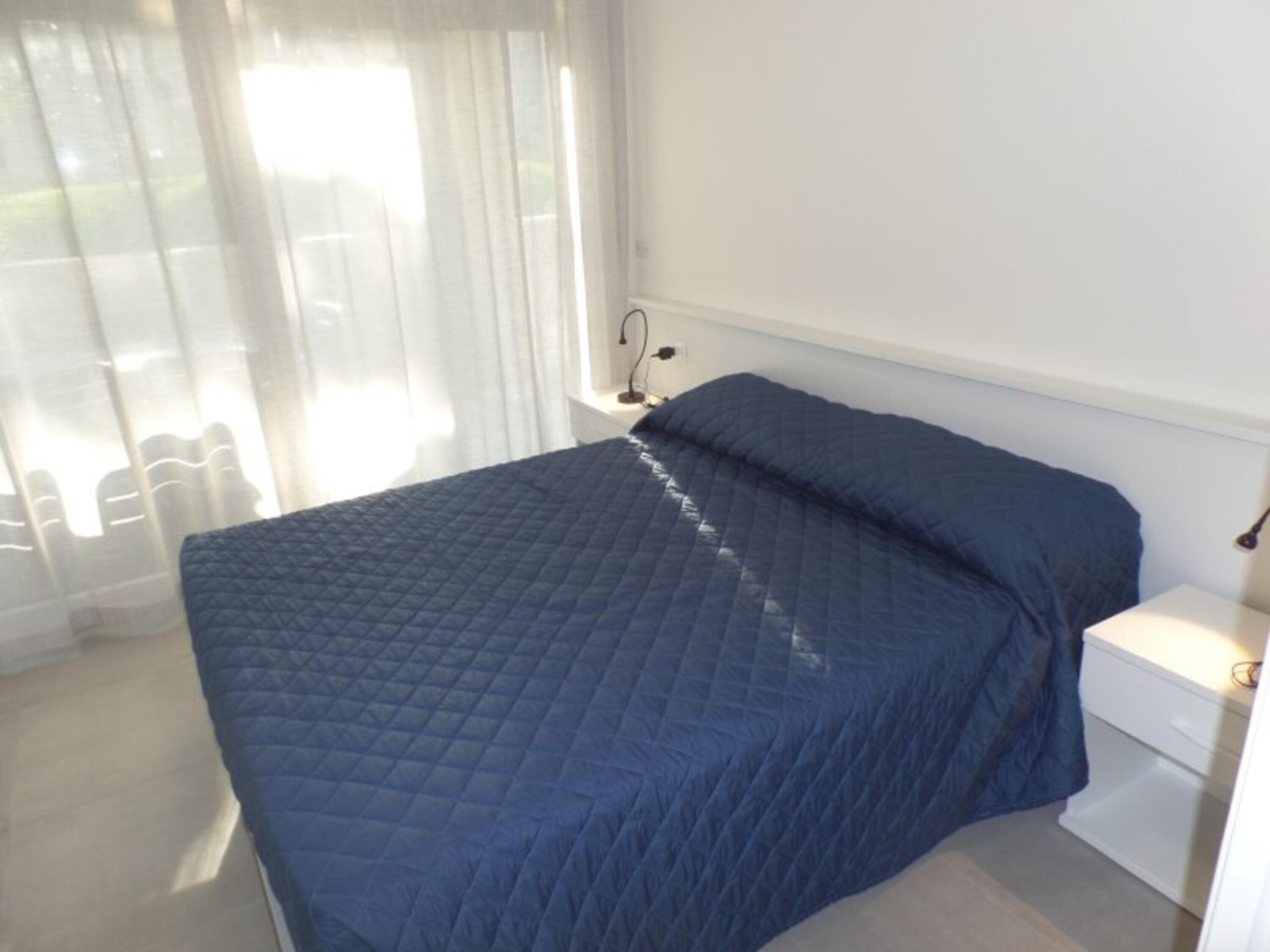 Una camera da letto con un letto, un comodino, una lampada e una finestra con tende.
