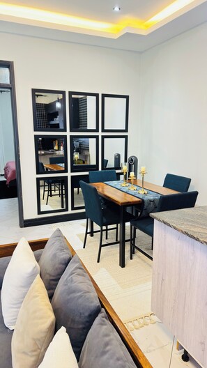 Ein modernes Wohnzimmer mit Essbereich, ausgestattet mit einer Couch, einem Esstisch mit Stühlen und einer durch eine Glasabtrennung sichtbaren Küche.
