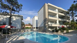 En modern byggnad med en swimmingpool, solstolar och parasoller.