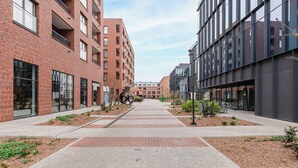 A modern urban street with brick buildings, a paved walkway, and small landscaped areas. - ShortStayPoland Szwedzka B196 (Warszawa)