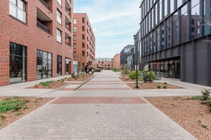 Eine moderne Stadtstraße mit Ziegelgebäuden, einem gepflasterten Gehweg und kleinen Grünflächen.